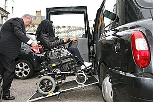 Taxiste poussant un fauteuil roulant pour le faire monter dand son taxi